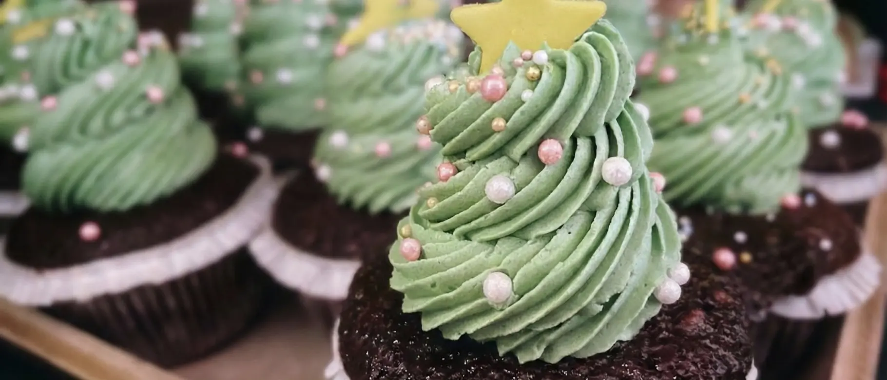 Foto eines Tellers mit mehreren Cupcakes, verziert mit grünem Frosting in Tannenbaumform. Das Bild dient als visuelle Metapher für die süße Verlockung von unregulierten "grünen" Werbeaussagen (Green Claims) im Vergleich zu Zucker, wie im Blogartikel beschrieben.