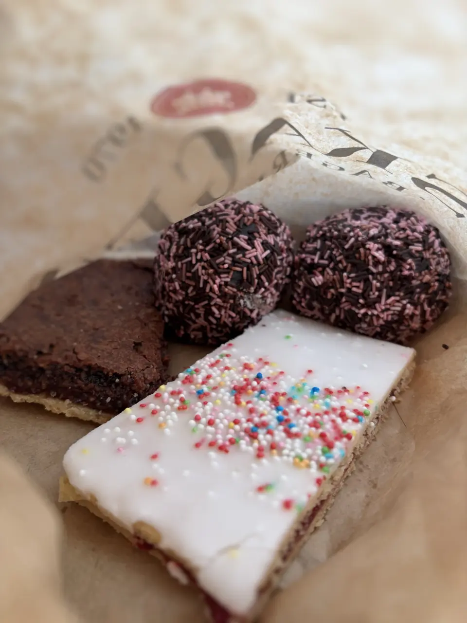 Close-up Foto in eine geöffnete Konditor-Papiertüte. Darin liegen eine Himbeerschnitte mit Zuckerguss und eine Rumkugel. Das Bild symbolisiert die Notwendigkeit von Transparenz bei Green Claims: Man muss wissen, was wirklich in der "Verpackung" (dem Produkt oder der Aussage) steckt, wie im Blogartikel thematisiert.