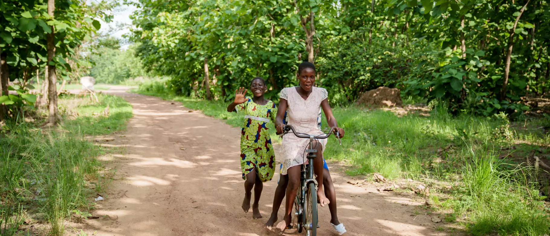 Zwei lachende Mädchen mit einem Fahrrad im PROJECT TOGO: Unterstützung der Mobilität und Bildungschancen durch die Fahrrad-Spendenaktion des ecocent e.V. in Westafrika.