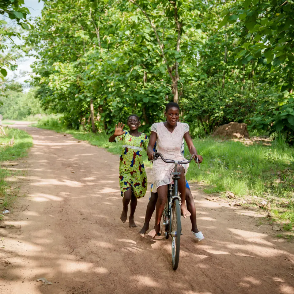 Zwei lachende Mädchen mit einem Fahrrad im PROJECT TOGO: Unterstützung der Mobilität und Bildungschancen durch die Fahrrad-Spendenaktion des ecocent e.V. in Westafrika.