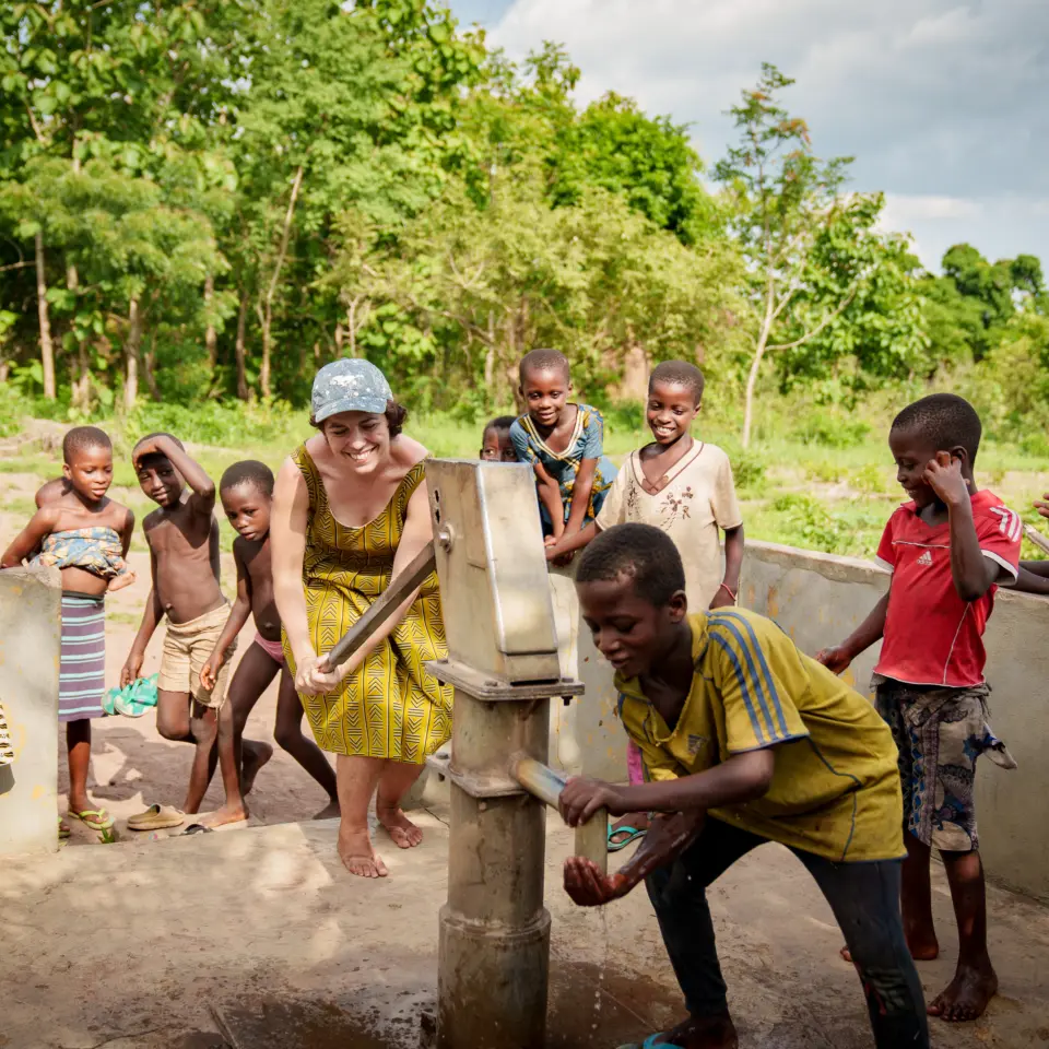 Kinder und eine Mitarbeiterin freuen sich über sauberes Wasser an einem von natureOffice gebauten Pumpbrunnen in Togo: Förderung der lokalen Infrastruktur und Lebensqualität.