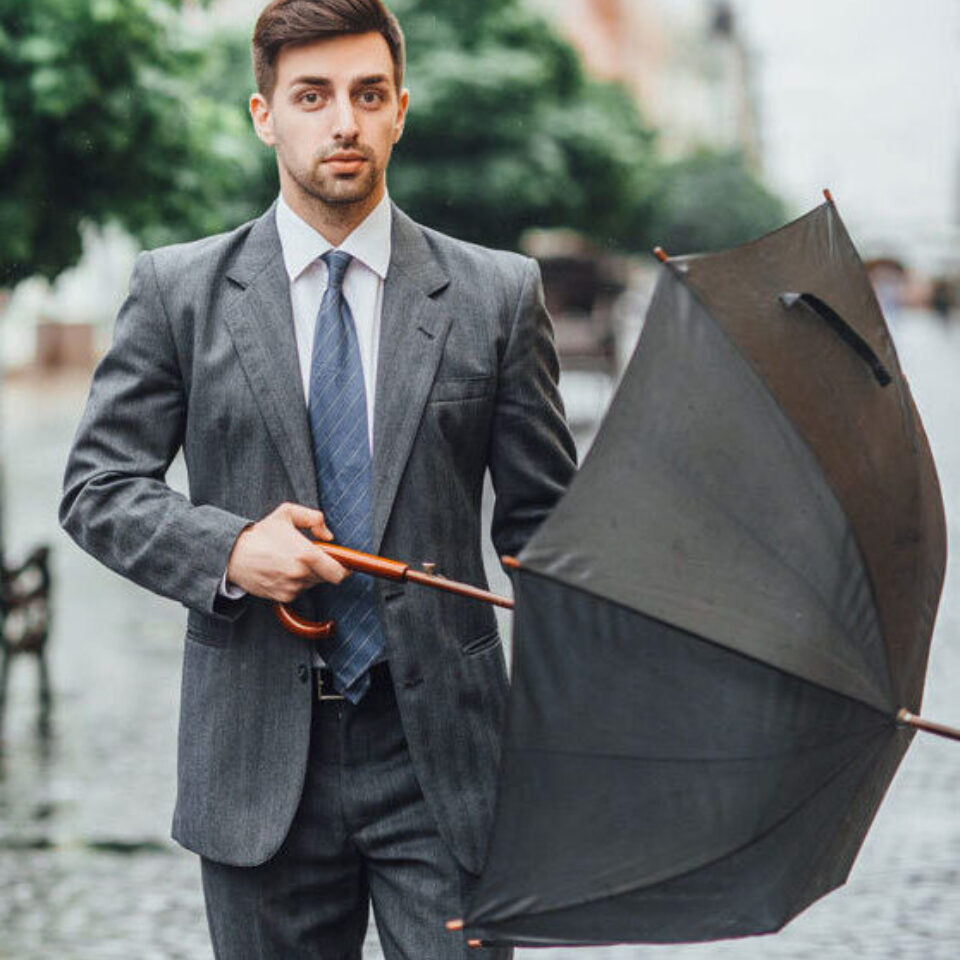 Ein Mann im Anzug geht mit einem Regenschirm in der Hand die Straße hinunter.