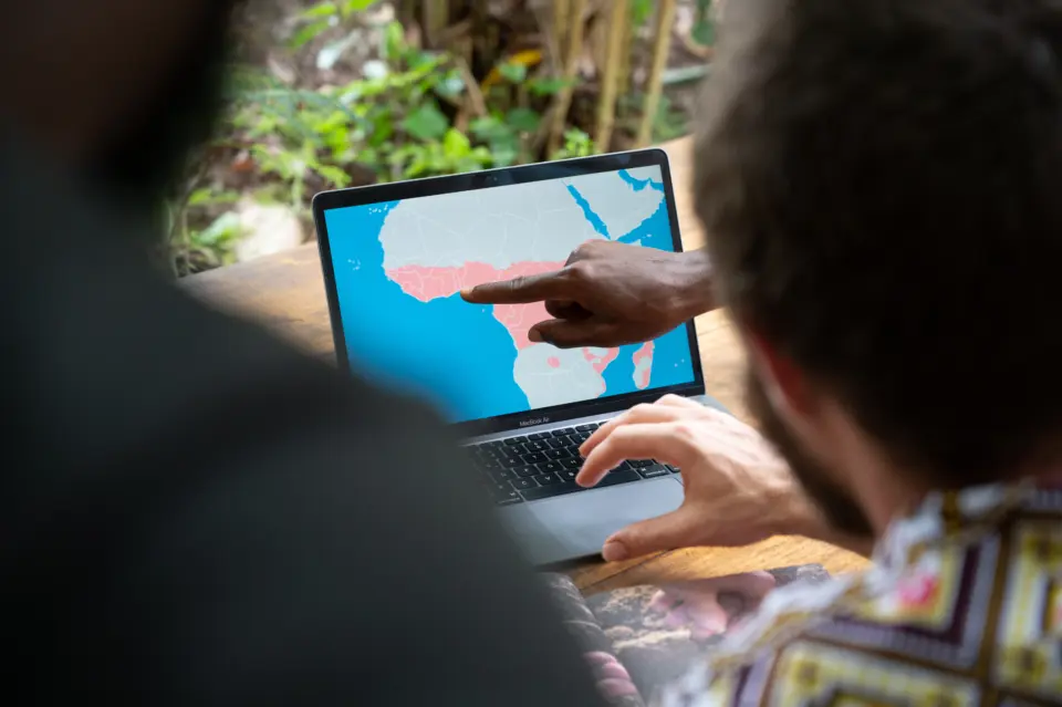 Digitale Transparenz im PROJECT TOGO: Ein Auditor zeigt während der Prüfung vor Ort den exakten Projektstandort auf einer digitalen Afrika-Karte am Laptop – Nachweis durch moderne Geodaten.