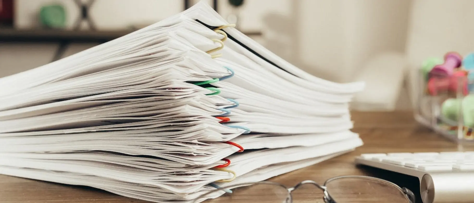 Several neatly stacked piles of paper with paper clips and a pair of reading glasses as a symbol of an audit-ready PCF evidence set for documenting CO₂ data.