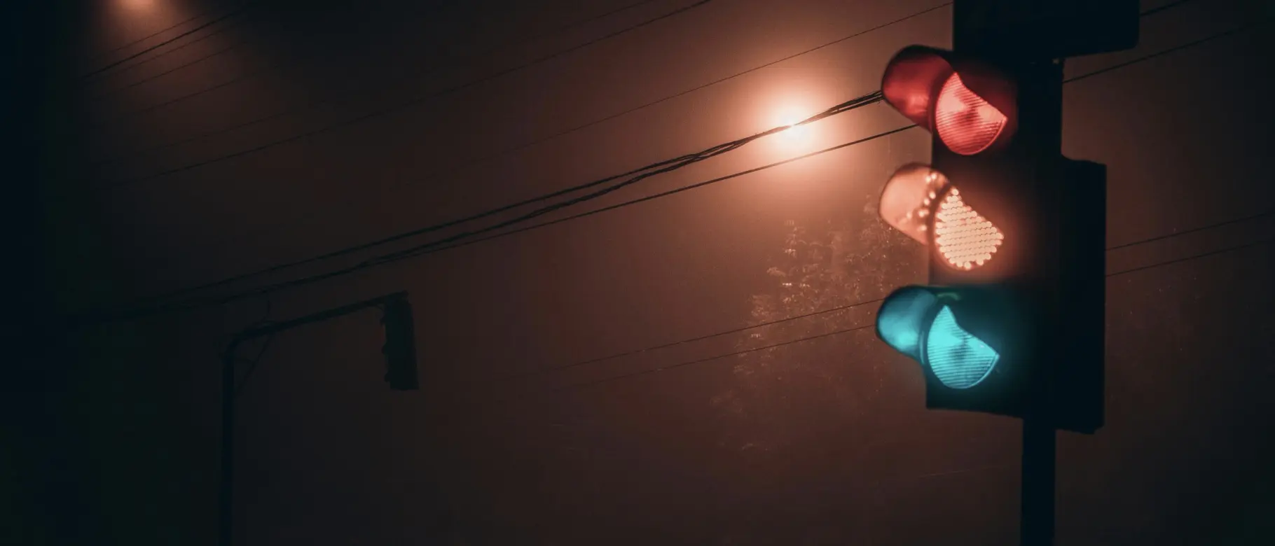 Ampel im Dunkeln mit gleichzeitig leuchtenden roten, gelben und grünen Lichtern – Symbol für die komplexen EU-Regeln rund um Climate Claims und Nachhaltigkeitskommunikation.