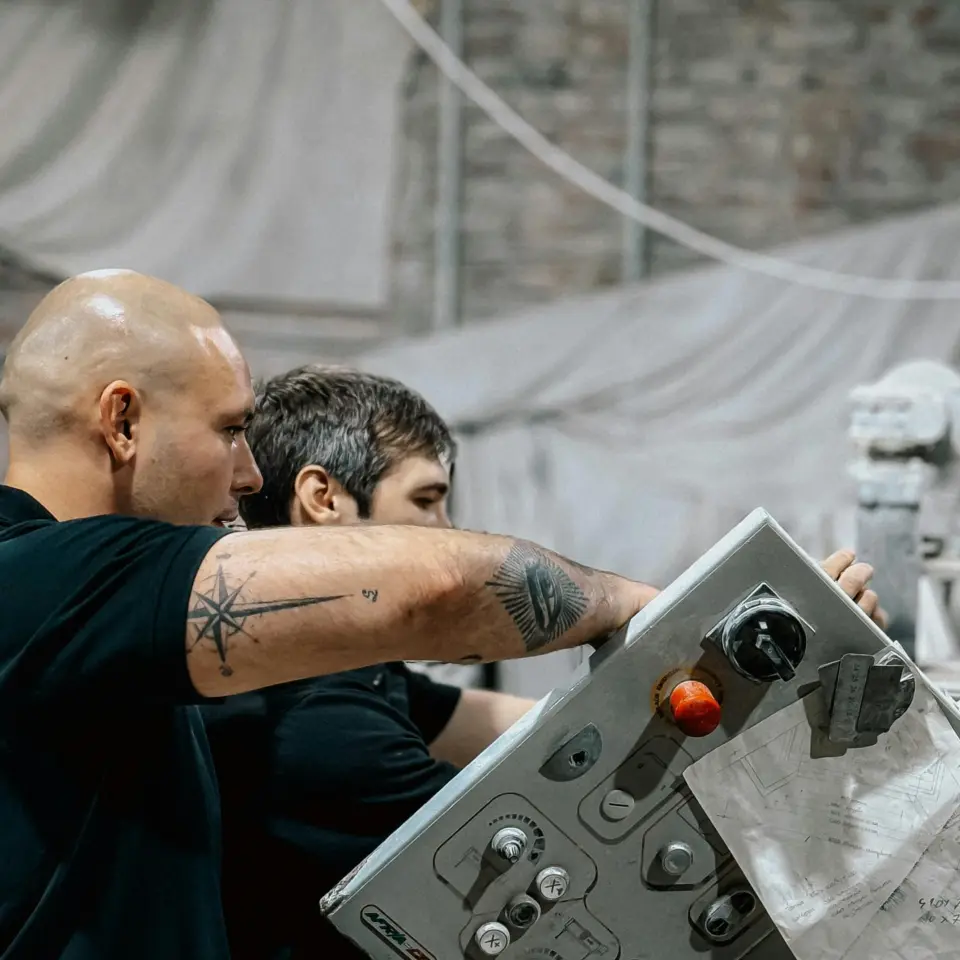 Two workers standing at a production machine monitoring an industrial manufacturing process